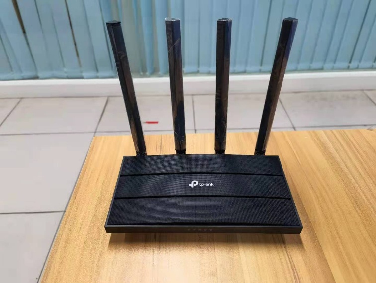 TP-Link router with four vertical antennas placed on a wooden table, front view.